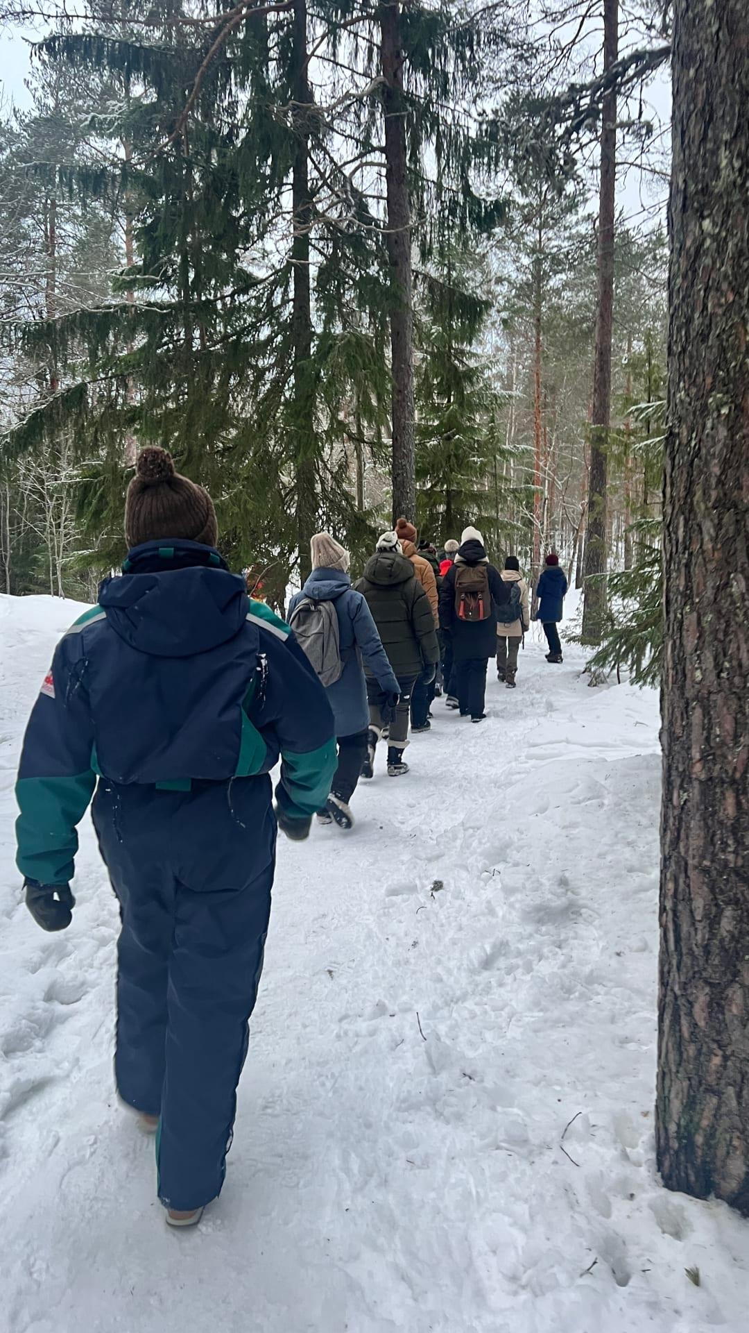 Ryhmä ihmisiä kävelee metsäpolkua talvella