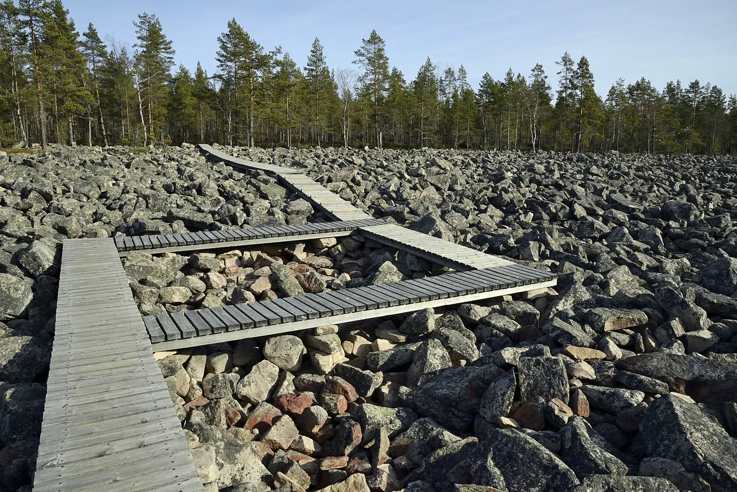 Kuva: Terttu Hermansson Kivilohkareita, joiden päälle on tehty puiset kulkuväylät. Taustalla metsä.