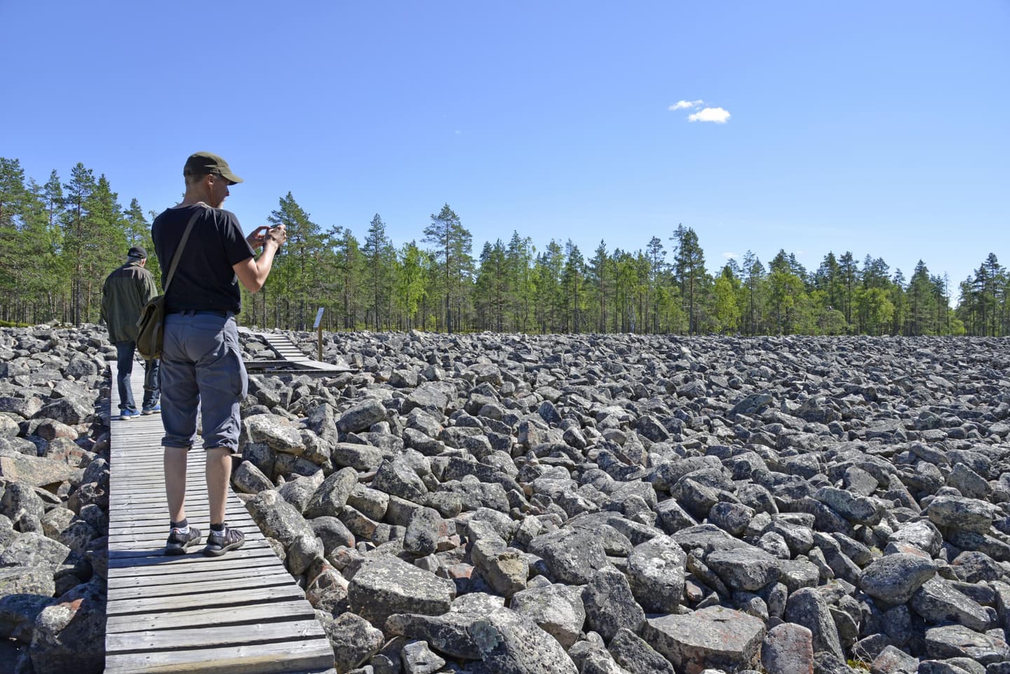 Kaksi miestä pitkospuilla. Etummainen mies ottaa kivistä kuvaa.