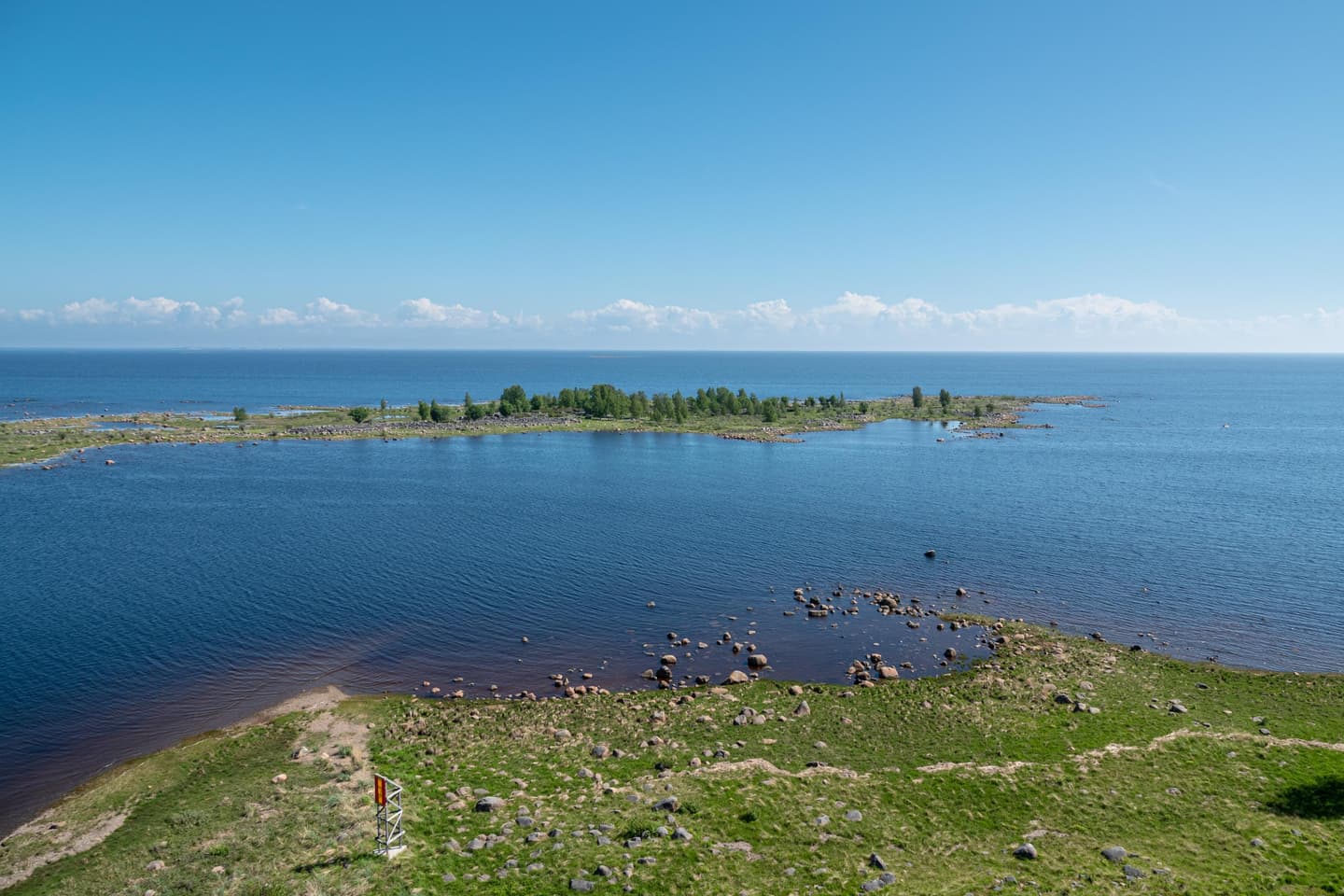 Kuva: Ismo Lampi Meri on tyyni ja taivas sininen. Etualalla maata ja kapean vesialueen vierellä saari.