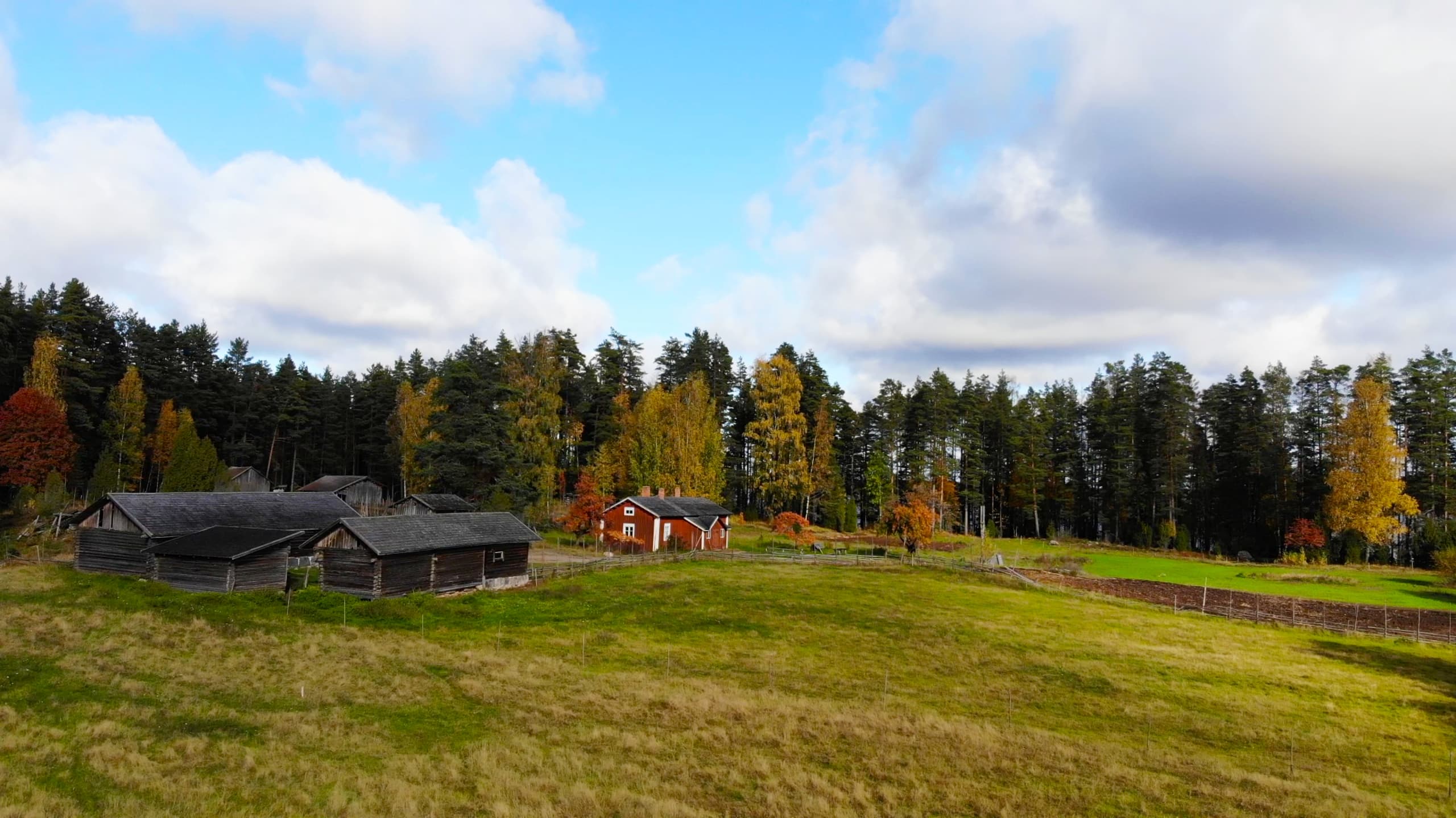 Kuva: Jaska Halttunen Perinnemaiseman etualalla avara laidun, jota reunustavat vanhat punaiset ja hirsiset maatalon rakennukset.