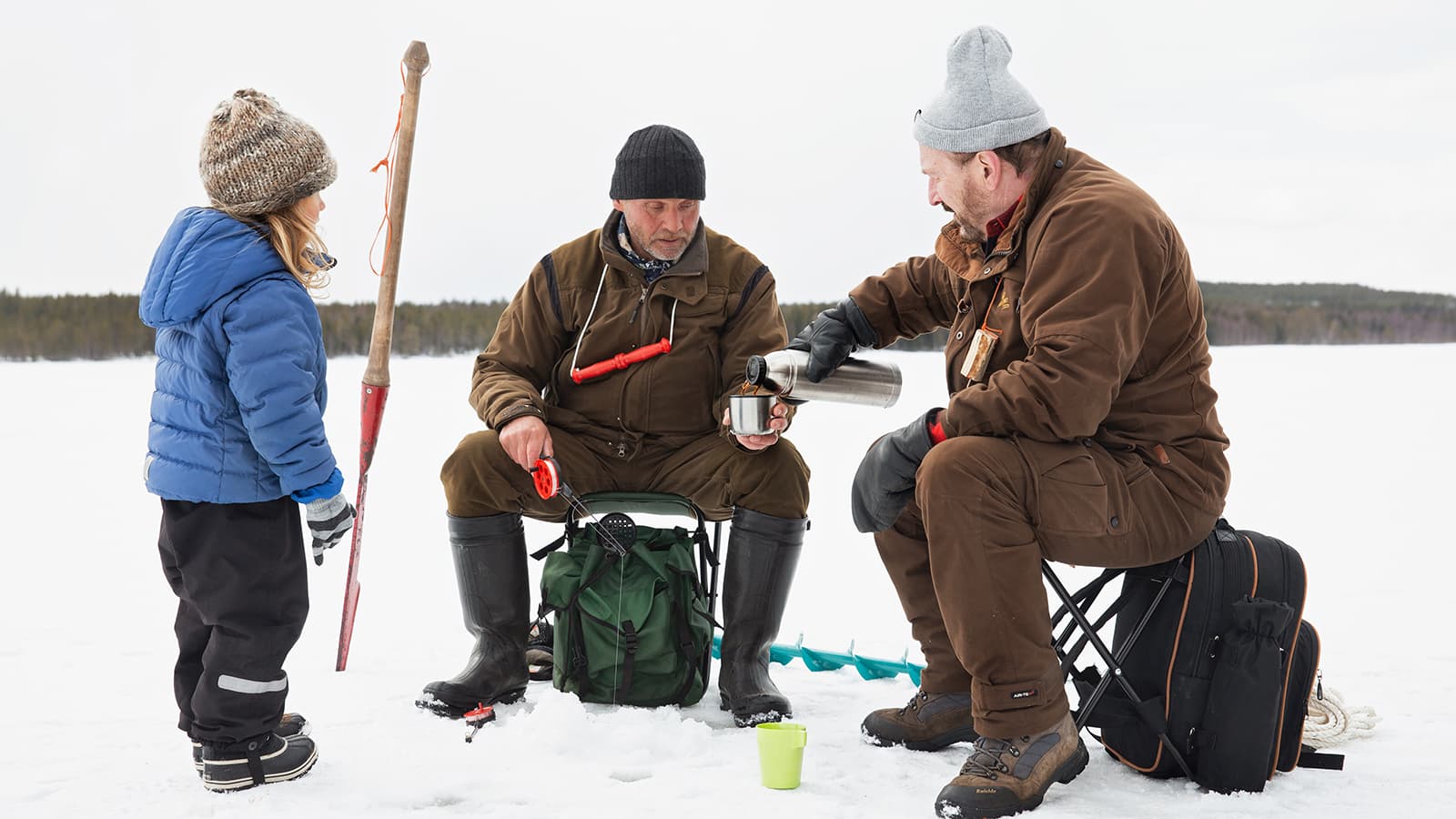 Image: Katri Lehtola / Keksi Two people are ice fishing and sitting on the ice on fishing stools, with a child standing next to them on the left.