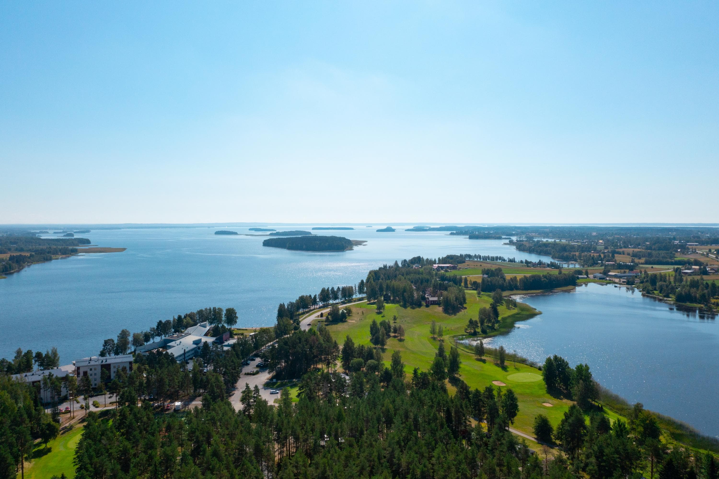 Kuva: Kraatterijärvi Geopark Ilmakuvassa kesäinen maisema kylän keskustasta ja sen takana aukeavasta järvestä.