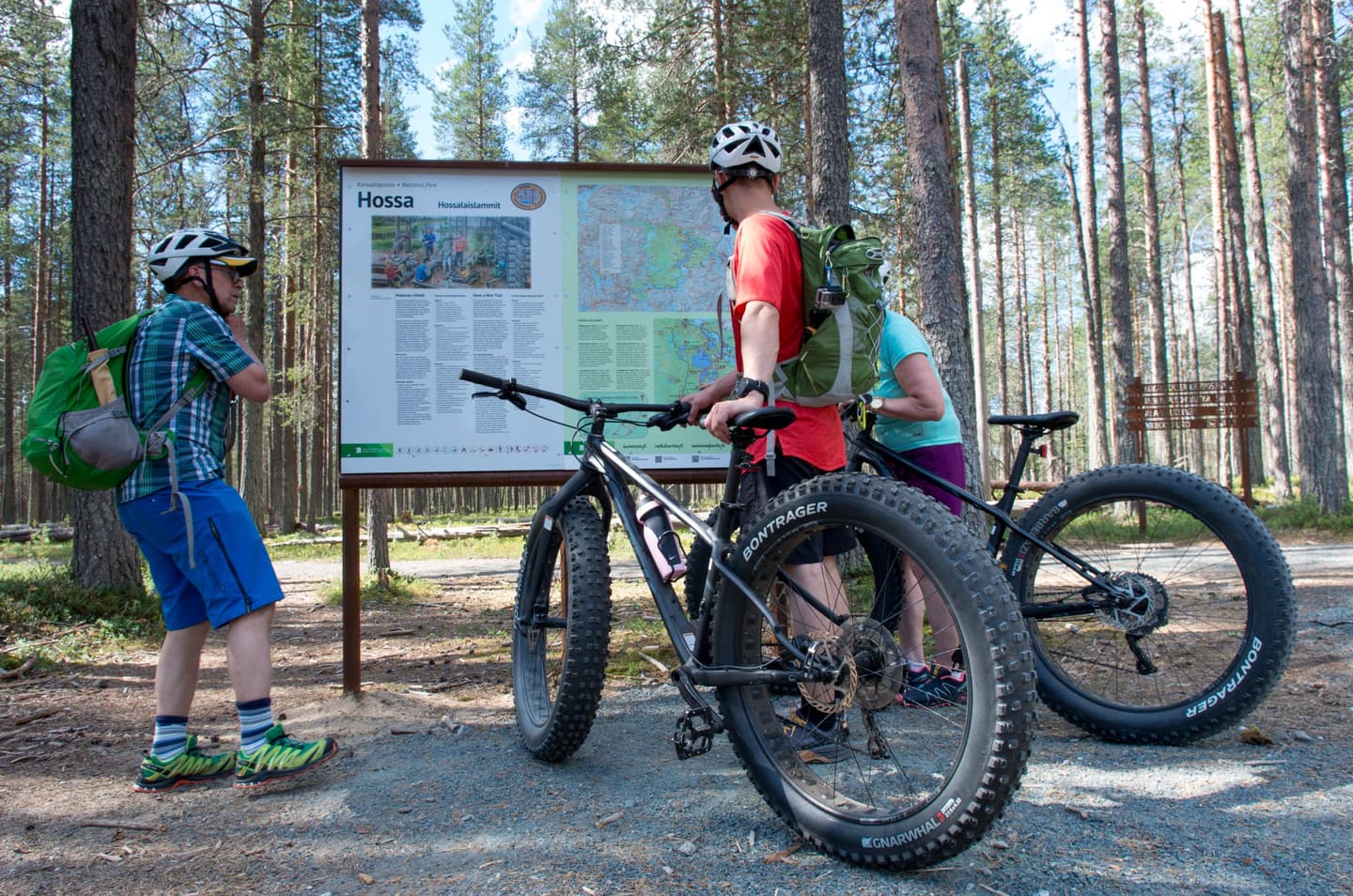 Image: Tuuli Turunen Mountain bikers next to an information board in summer. Forest in the background.
