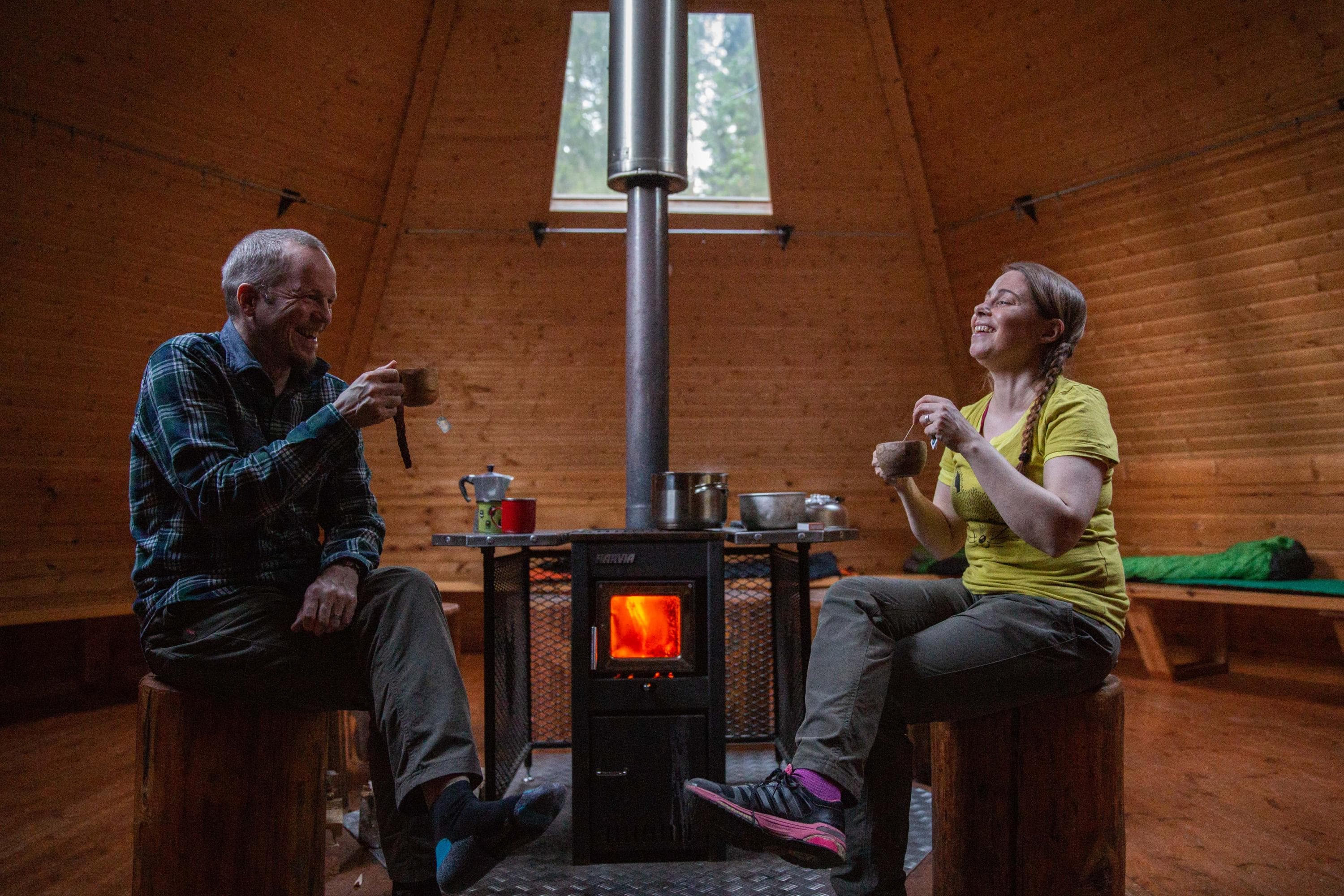 Bild: Saara Lavi. Kaksi retkeilijää istuu kodassa kamiinan äärellä.