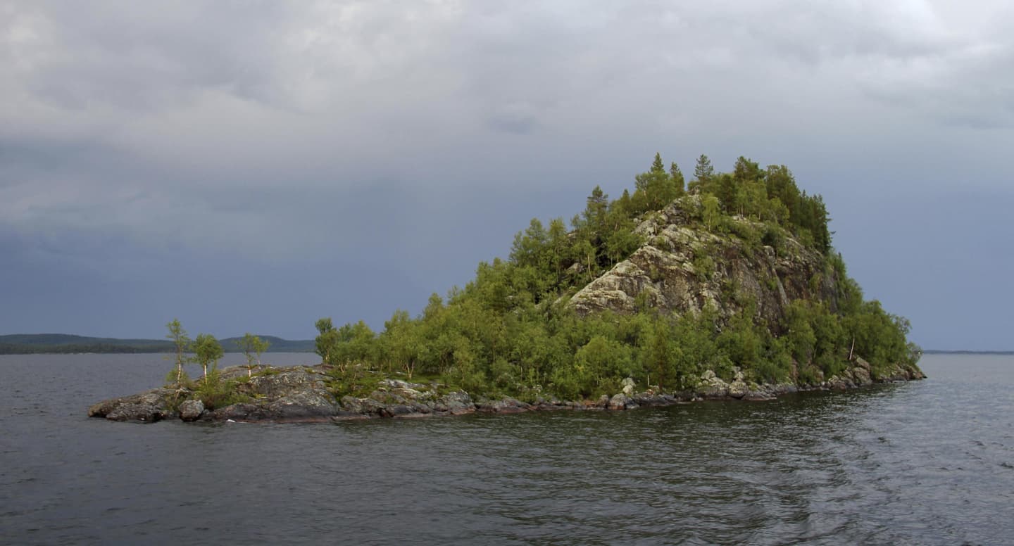Image: Pasi Nivasalo Från ena änden platt och från andra änden en hög klippö omgiven av vatten. Ön är delvis täckt av gröna träd.