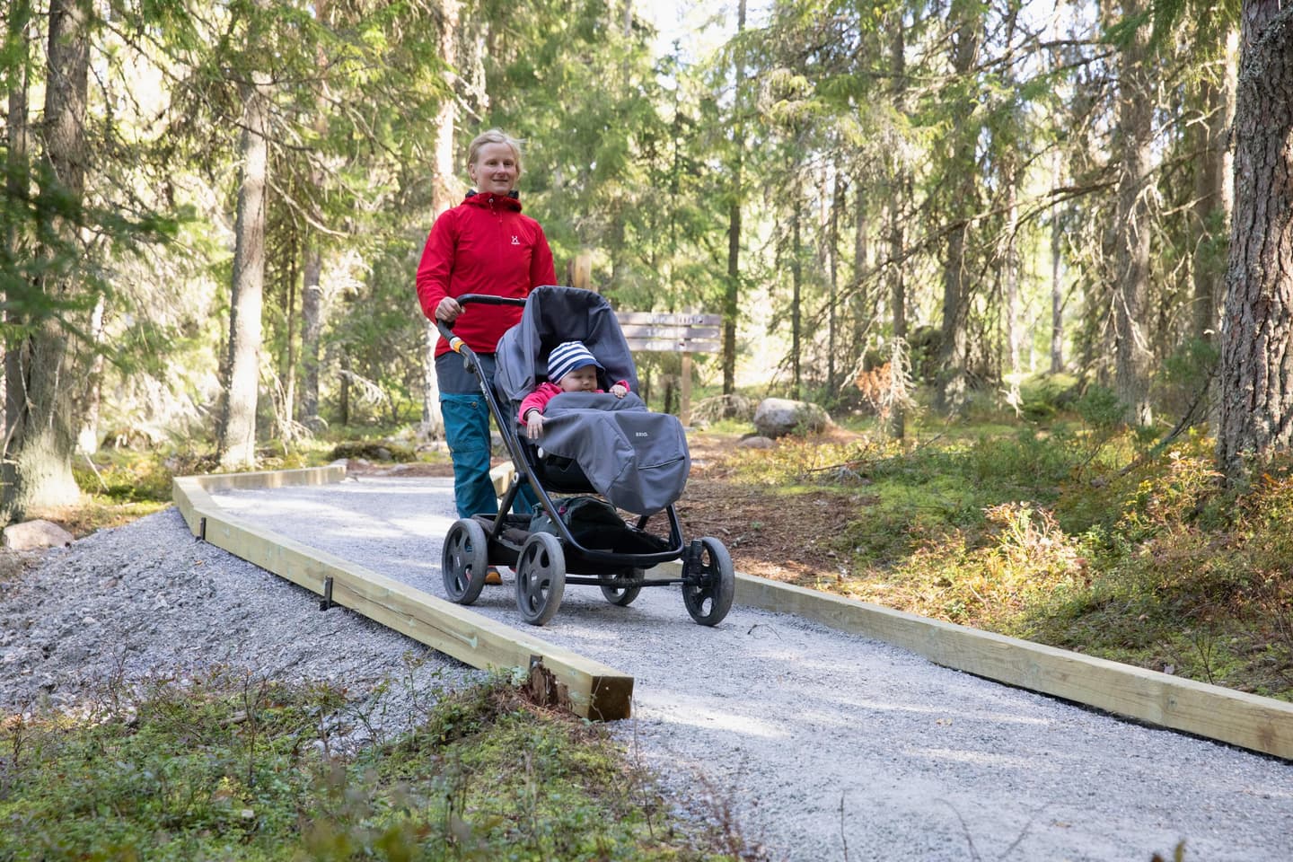 Image: Katri Lehtola Woman walks with a pram along the trail. There is forest on both side of the trail.