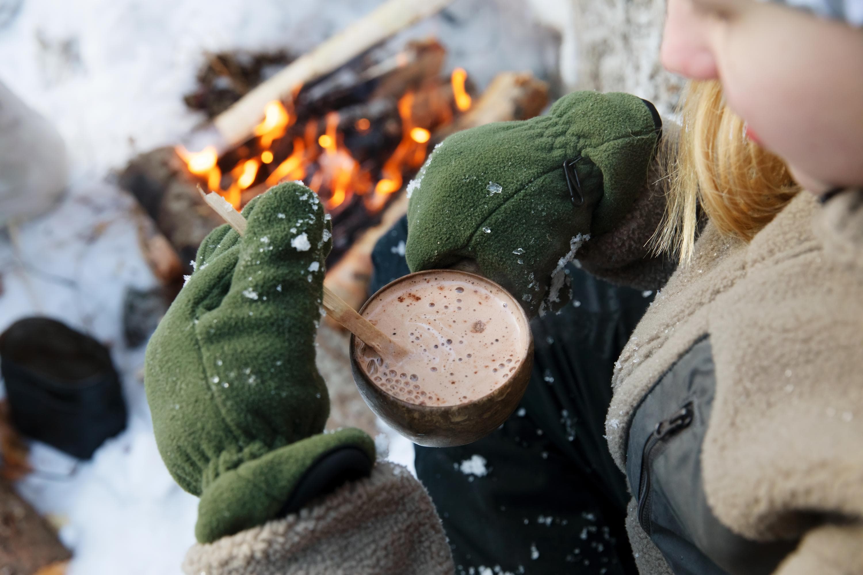 Image: Katri Lehtola A girl is by the fire in winter. She is holding a mug of hot cocoa in her hands.