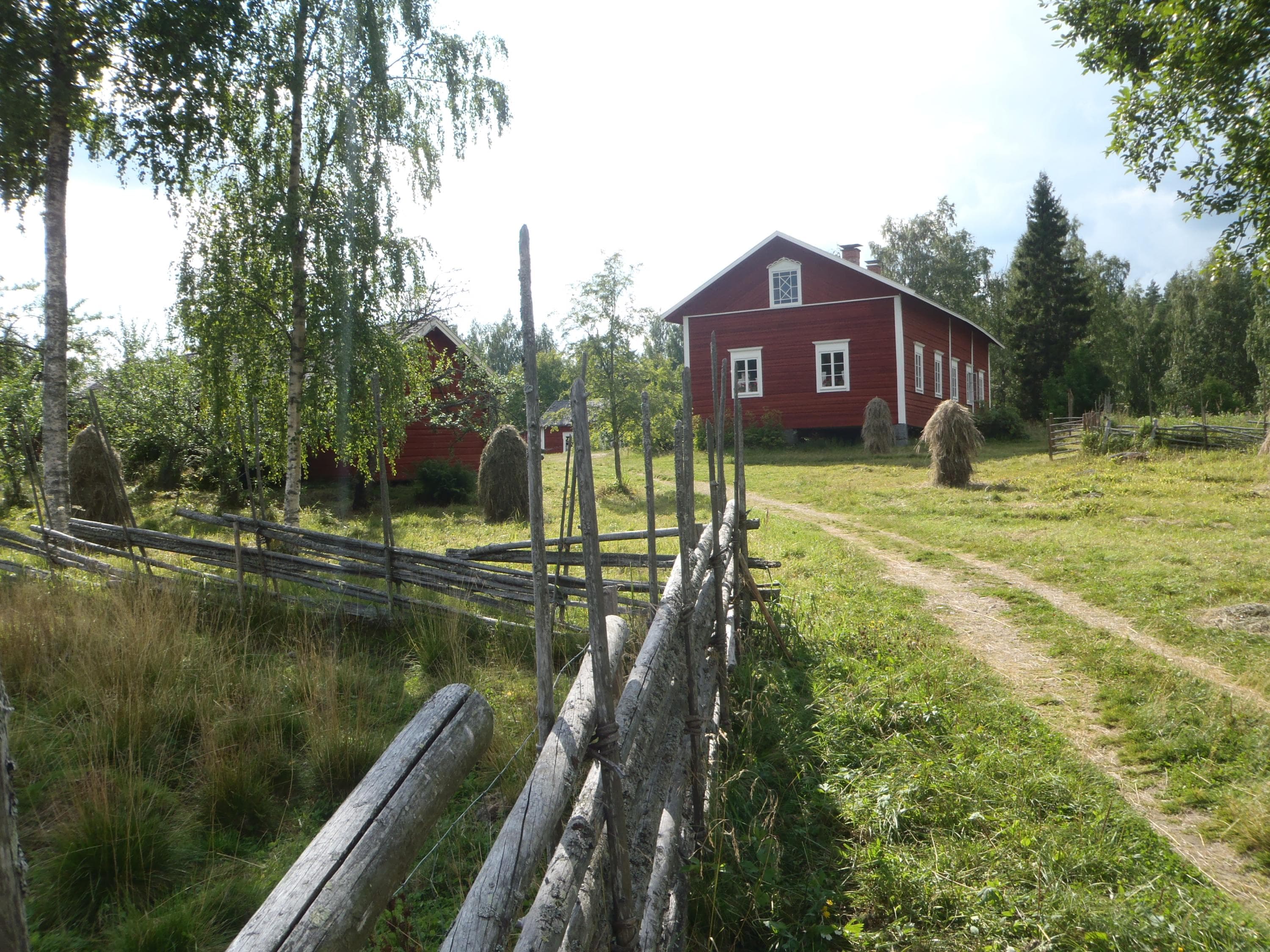 Kuva: Leena Hiltunen Punainen hirsirakennus. Kuvan edustalla on riukuaita.