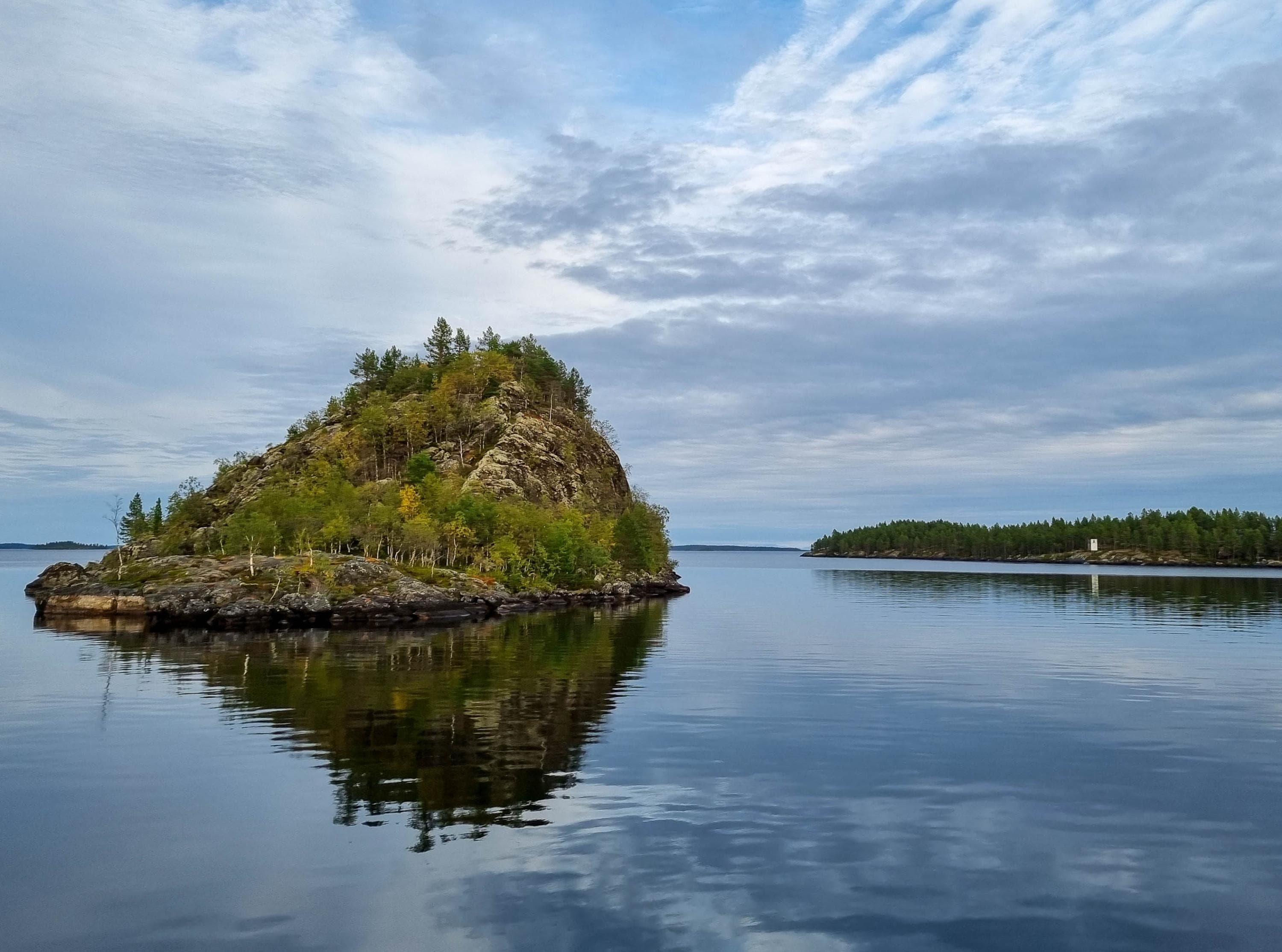 Image: Kirsi Ukkonen An island shaped like an anthill is reflected on the still water.