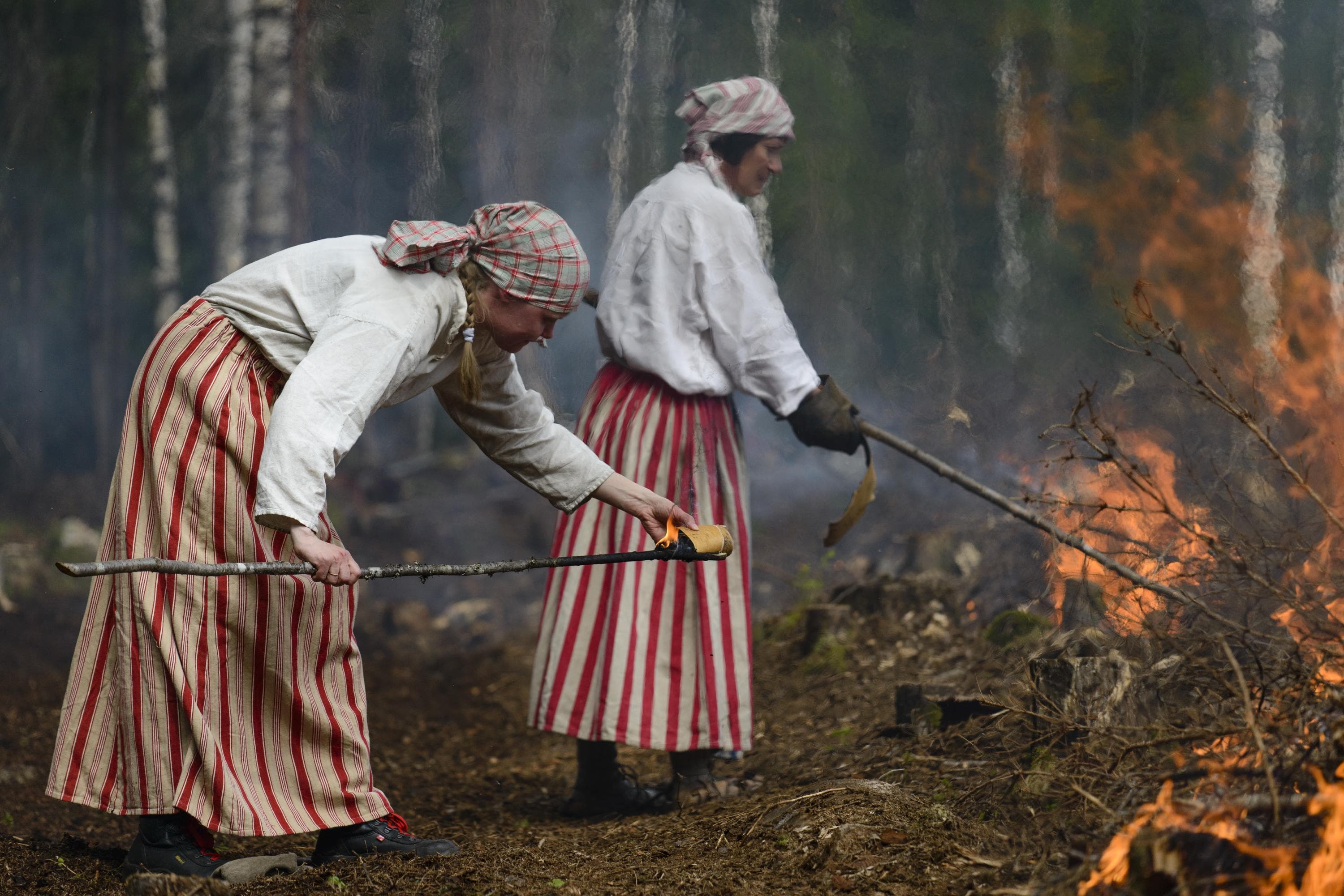 Kuva: Marko Haapalehto Kaksi punaraidallisiin hameisiin pukeutunutta henkilöä sytyttämässä kaskea.