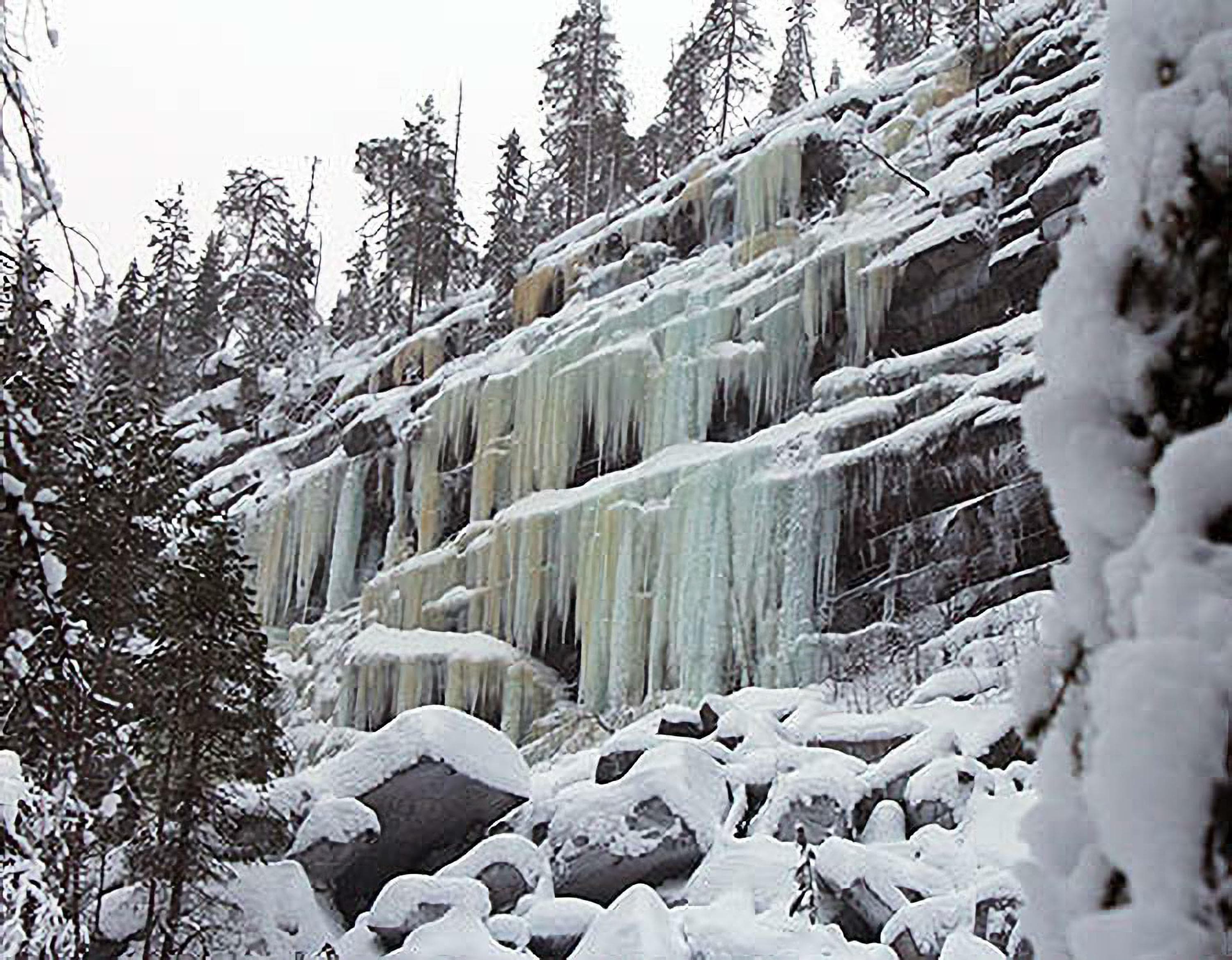 Kuva: Pekka Veteläinen Monikerroksinen jääputous. Kallioiden päällä on puita ja keli on harmaa.