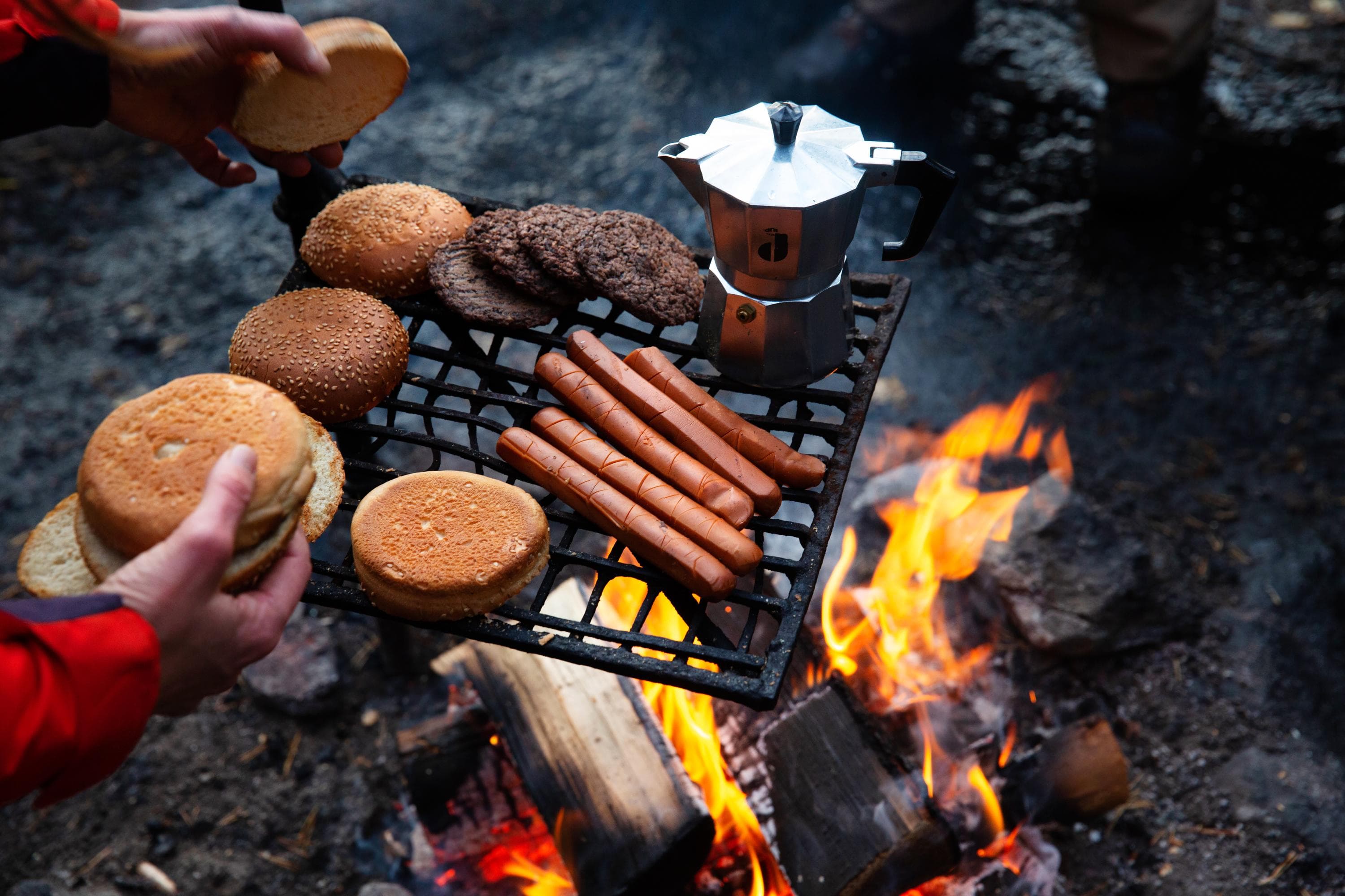 Kuva: Katri Lehtola Retkeilijöiden eväitä nuotiolla. Ritilän päällä hampurilaisaineksia ja kahvipannu.