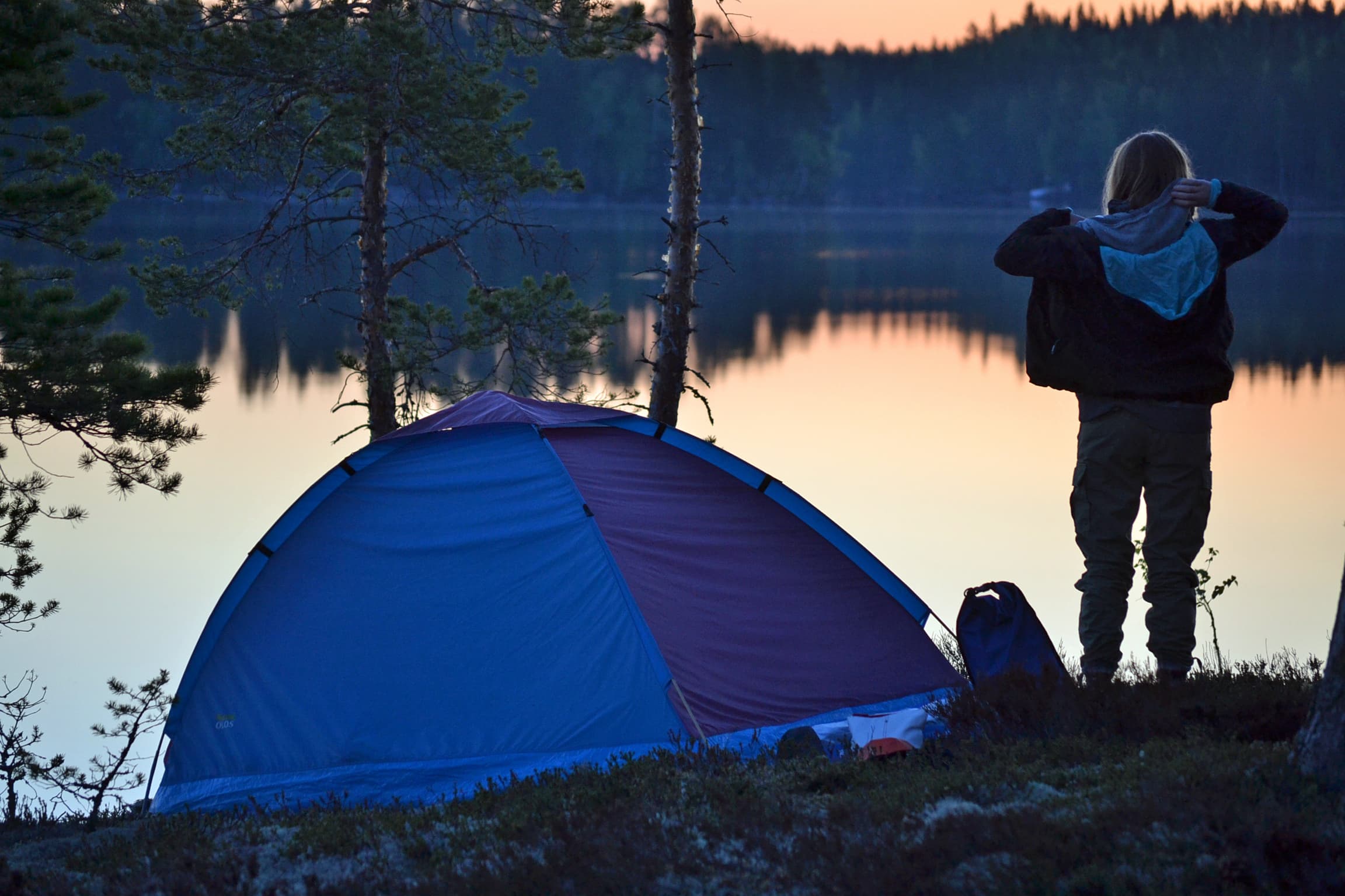 Image: Janita Juvakka A camper stands by the shore next to their tent on a summer evening.