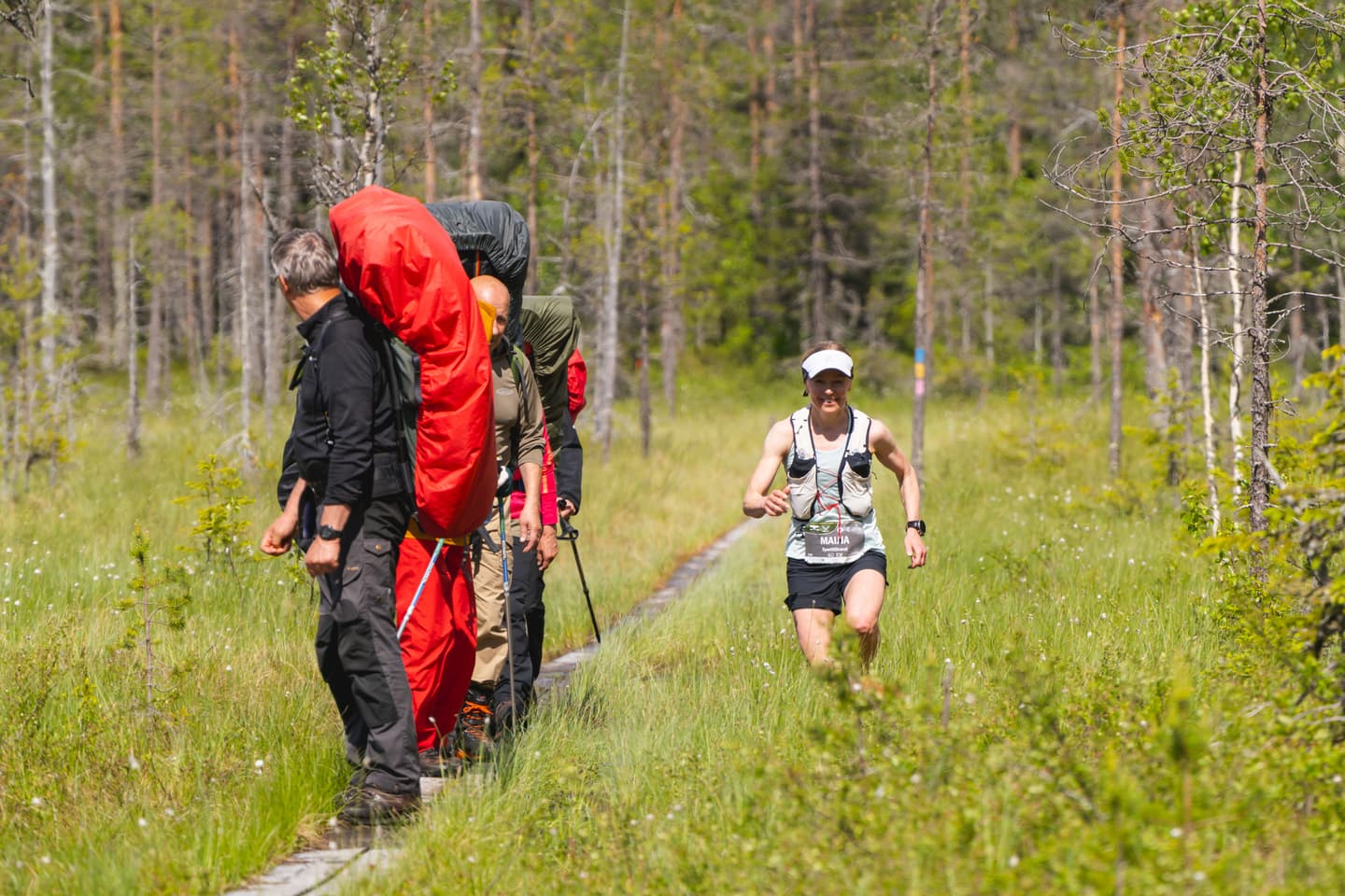 Kuva: Rami Valonen Retkeilijöitä pitkospuilla rinkat selässä, joita juoksija ohittaa suon kautta.