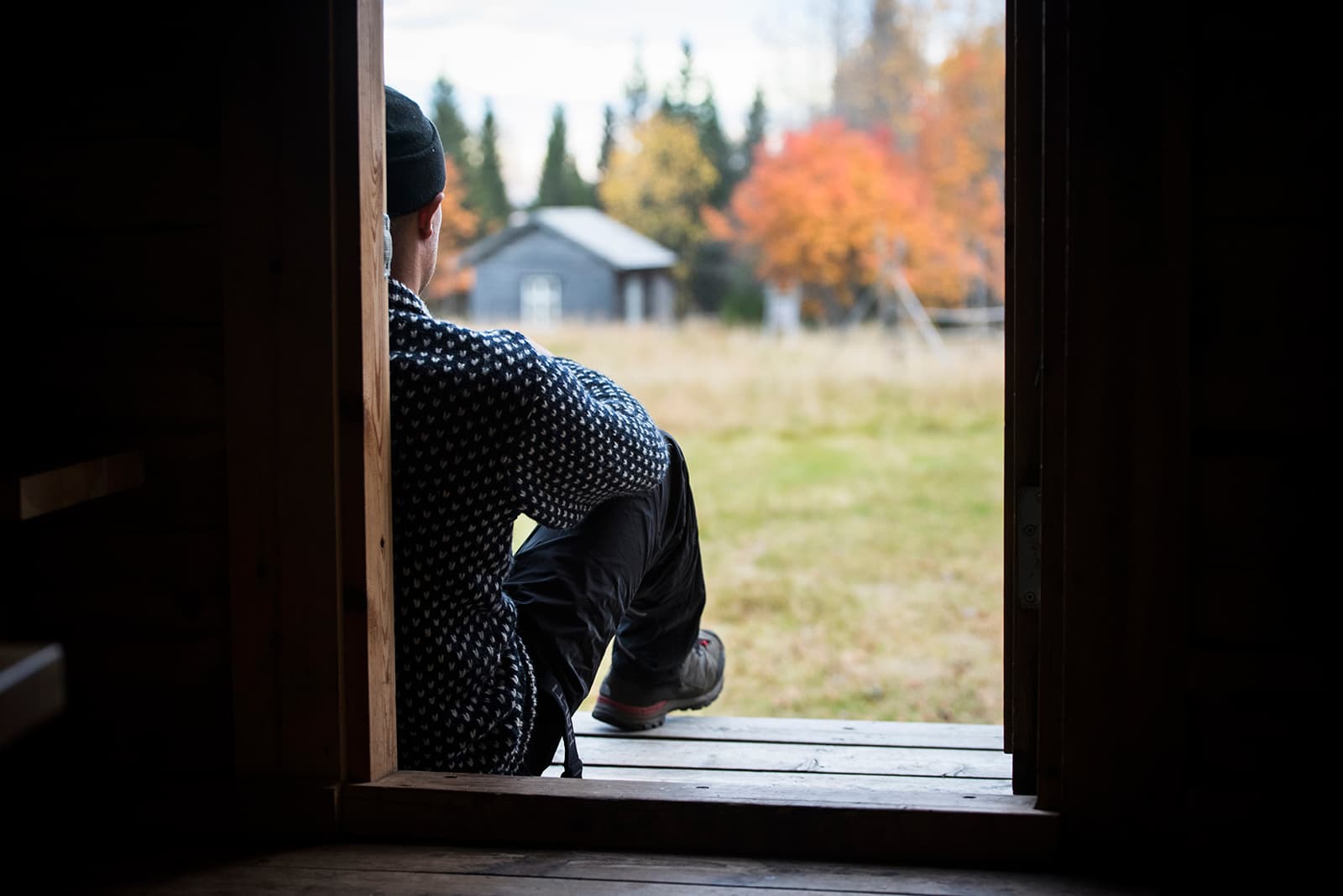 Bild: Eeva Mäkinen En person sitter på trappan till en byggnad. Genom dörröppningen syns en höstig gammal gårdsplan.