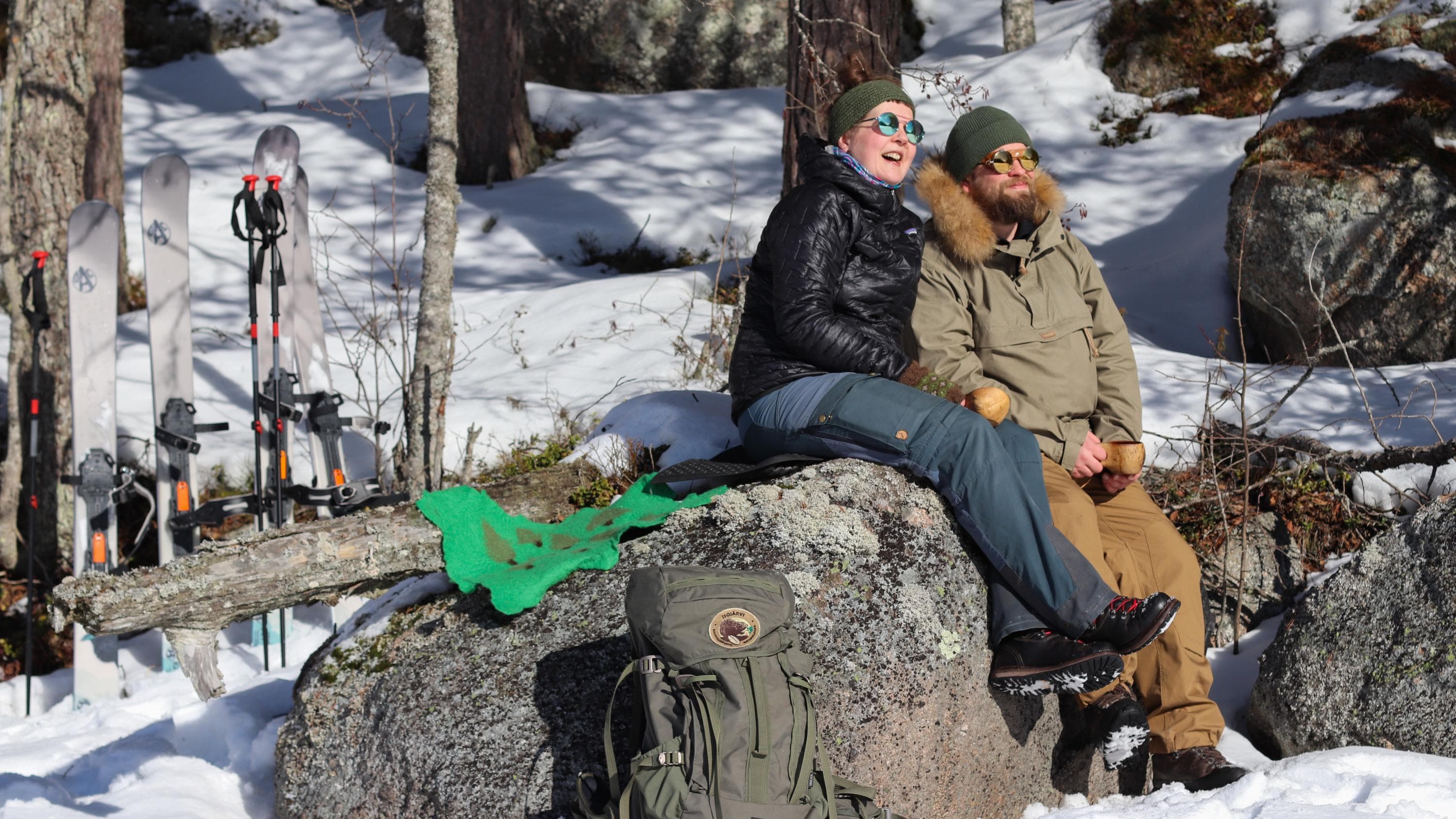 Kuva: Tommi Lehtinen Kaksi retkeilijää istuu suurella kivellä kevätauringossa. Maastossa on vielä lunta ja retkeilijät ovat liikenteessä liukulumikengillä.