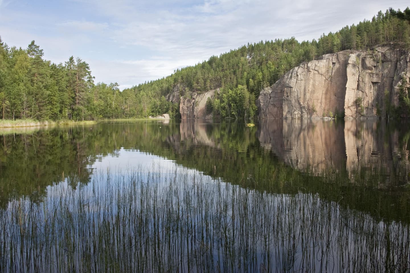 Image: Lassi Kujala A calm pond with a steep cliff rising behind it.